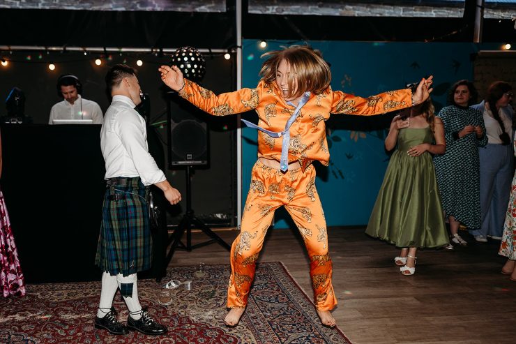 Woman jumping up and dancing bare foot in an orange suit that has leopards on it