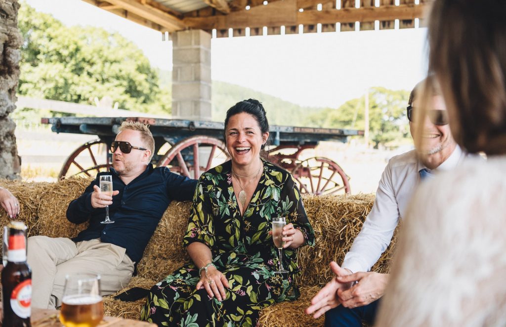 A group of people sat on hay bales drinking champagne smiling and laughing