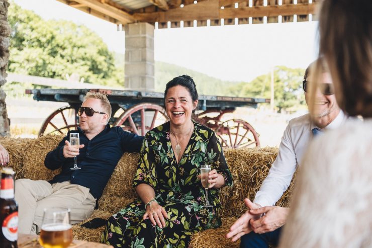 A group of people sat on hay bales drinking champagne smiling and laughing