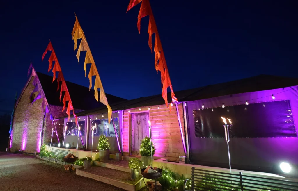 Outside of a barn lit up with pink lights, festival flags and stringed lights