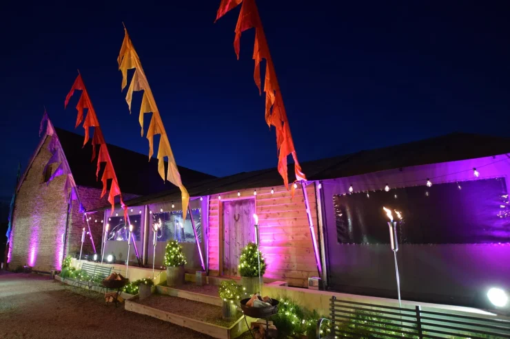 Outside of a barn lit up with pink lights, festival flags and stringed lights